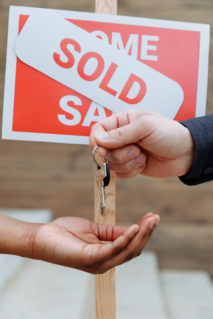 services-01 Hands exchanging house keys in front of a sold sign, symbolizing real estate success.